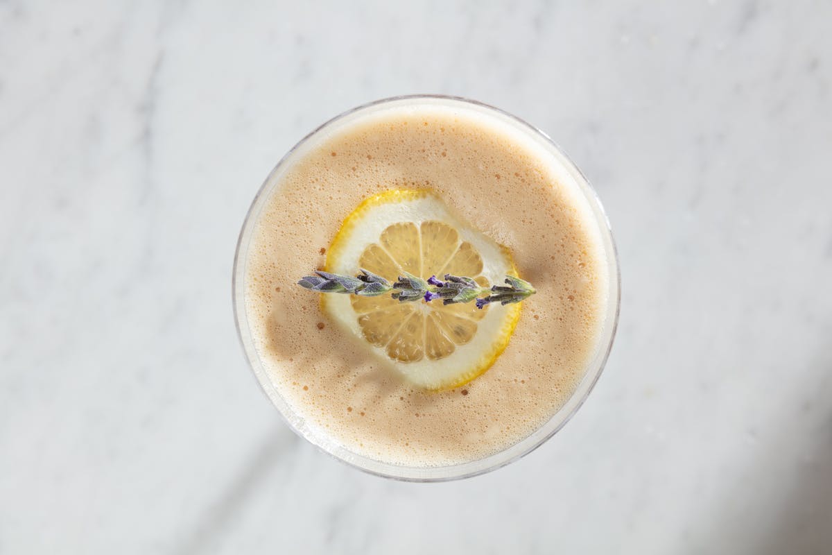 a cocktail with a lemon wedge and sprig of lavender